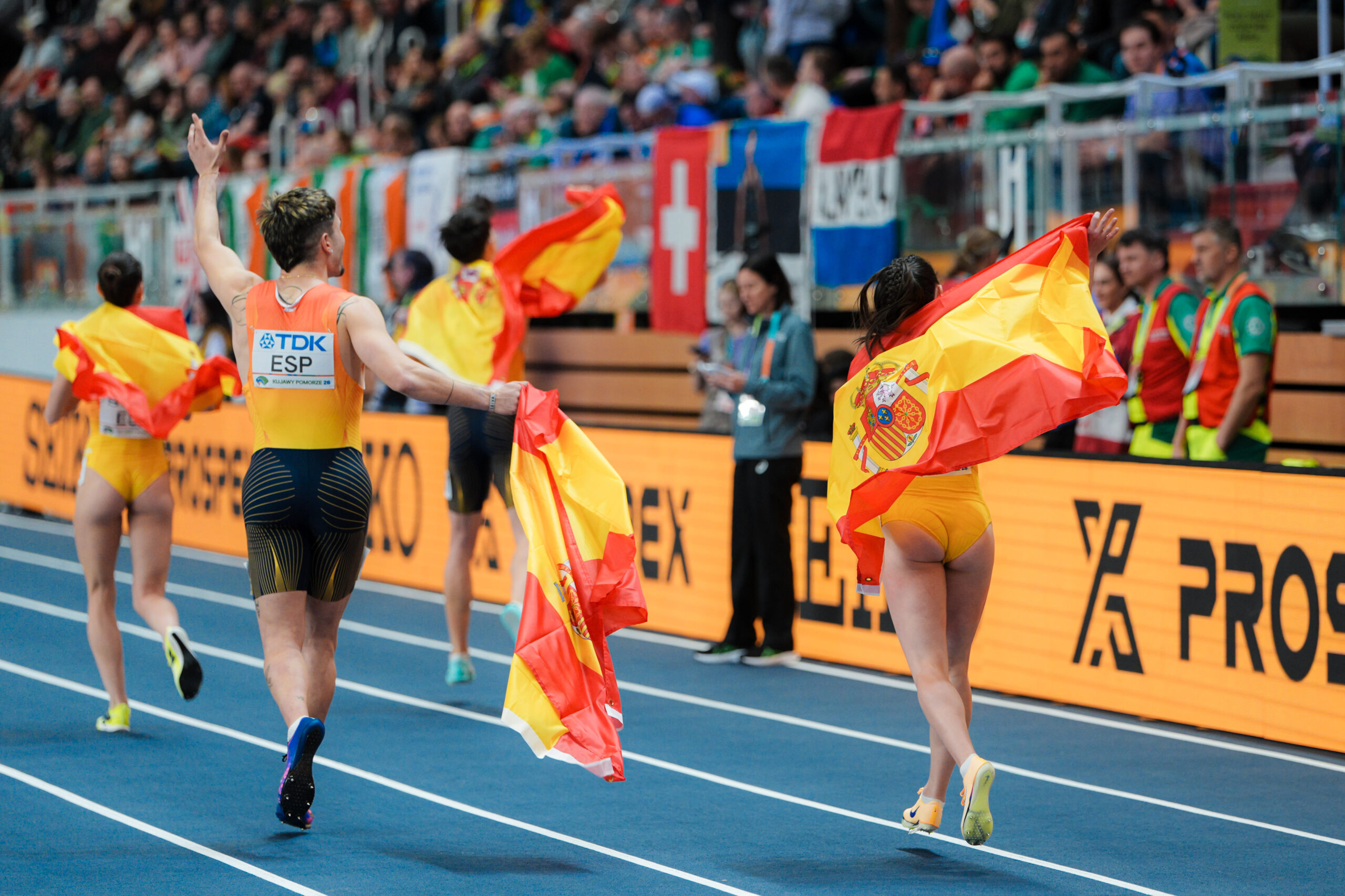 Markel Fernández y el equipo español de relevo 4x400 mixto celebrando su medalla con la bandera de España en la pista del Mundial de Toruń 2026.